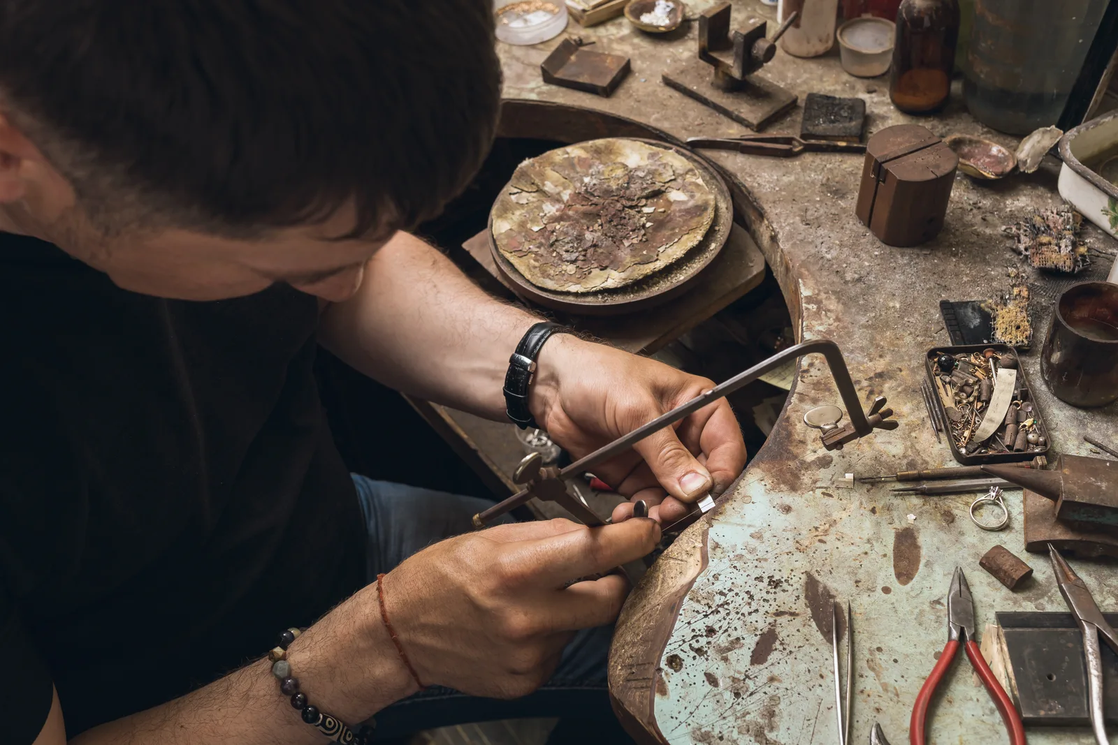 A goldsmith at the bench, sawing a small piece held against the bench pin