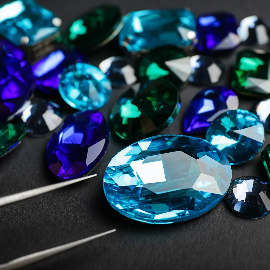 A scatter of blue and green gems with tweezers