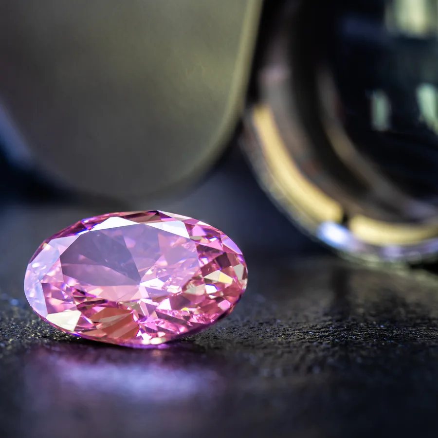 A pink oval gem beside a jeweler's loupe