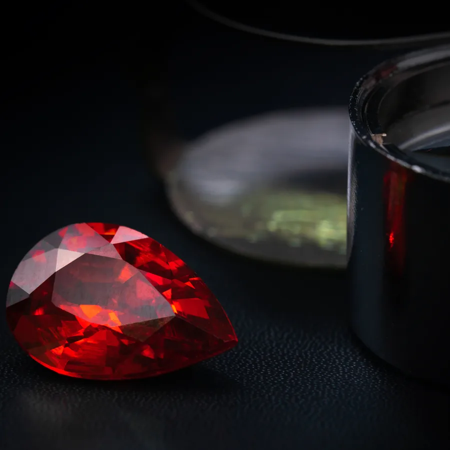 A red pear-shaped gem beside a loupe