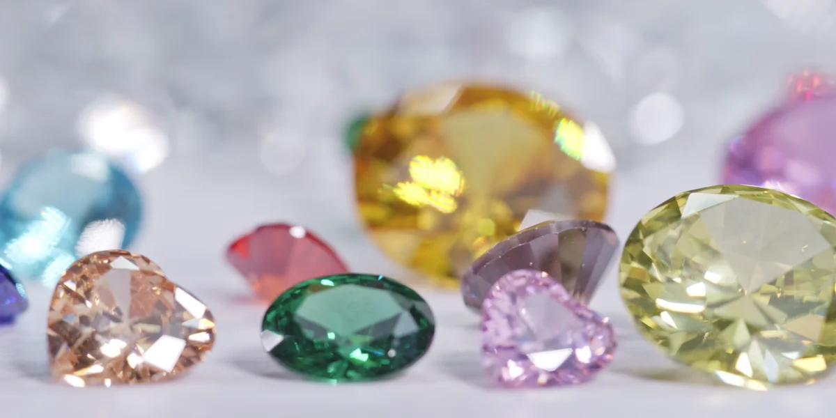 Loose colored gems: an emerald, a pink heart, a yellow oval and a peach heart at the front