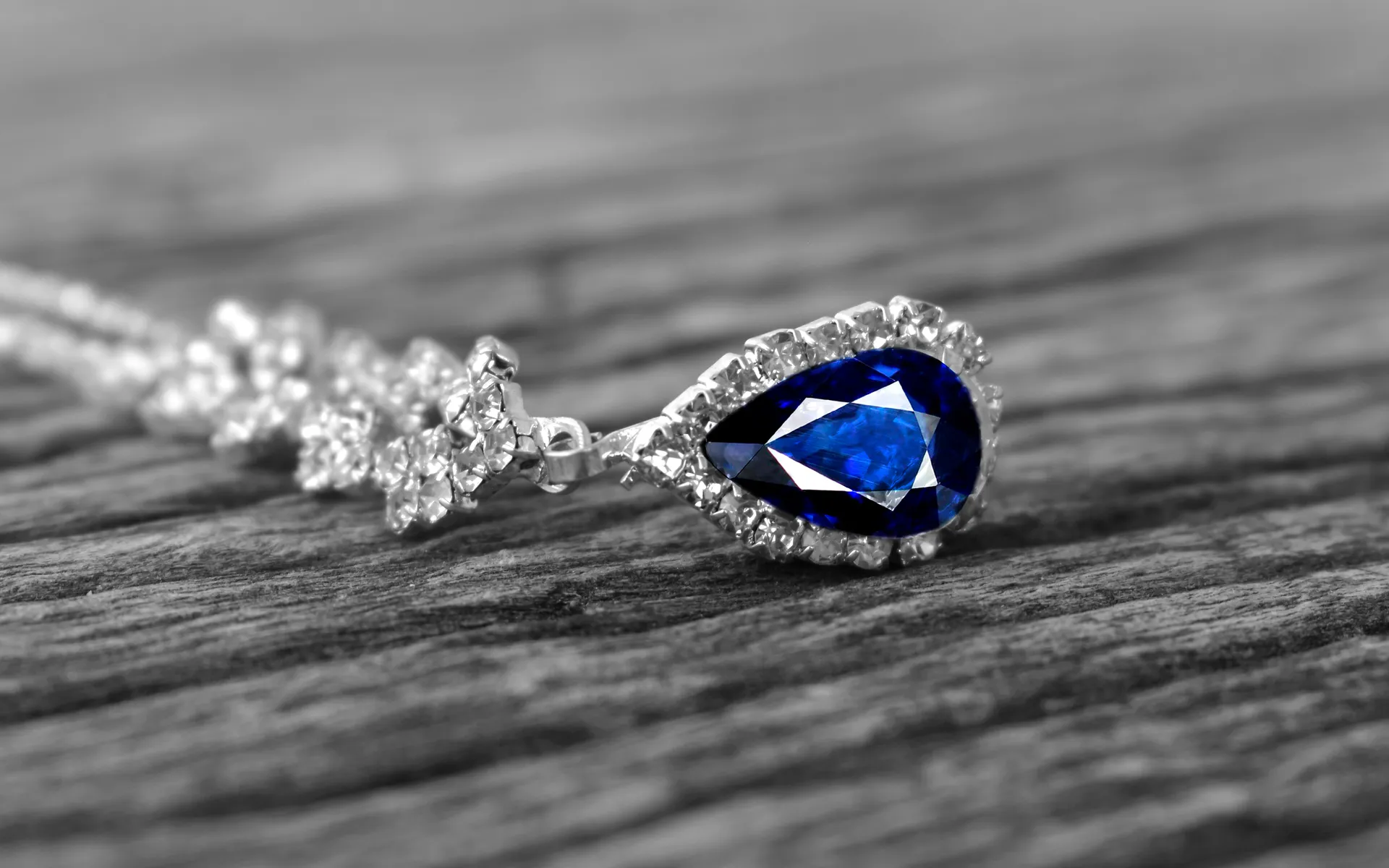 A pear-shaped sapphire pendant in a halo of diamonds, resting on weathered wood