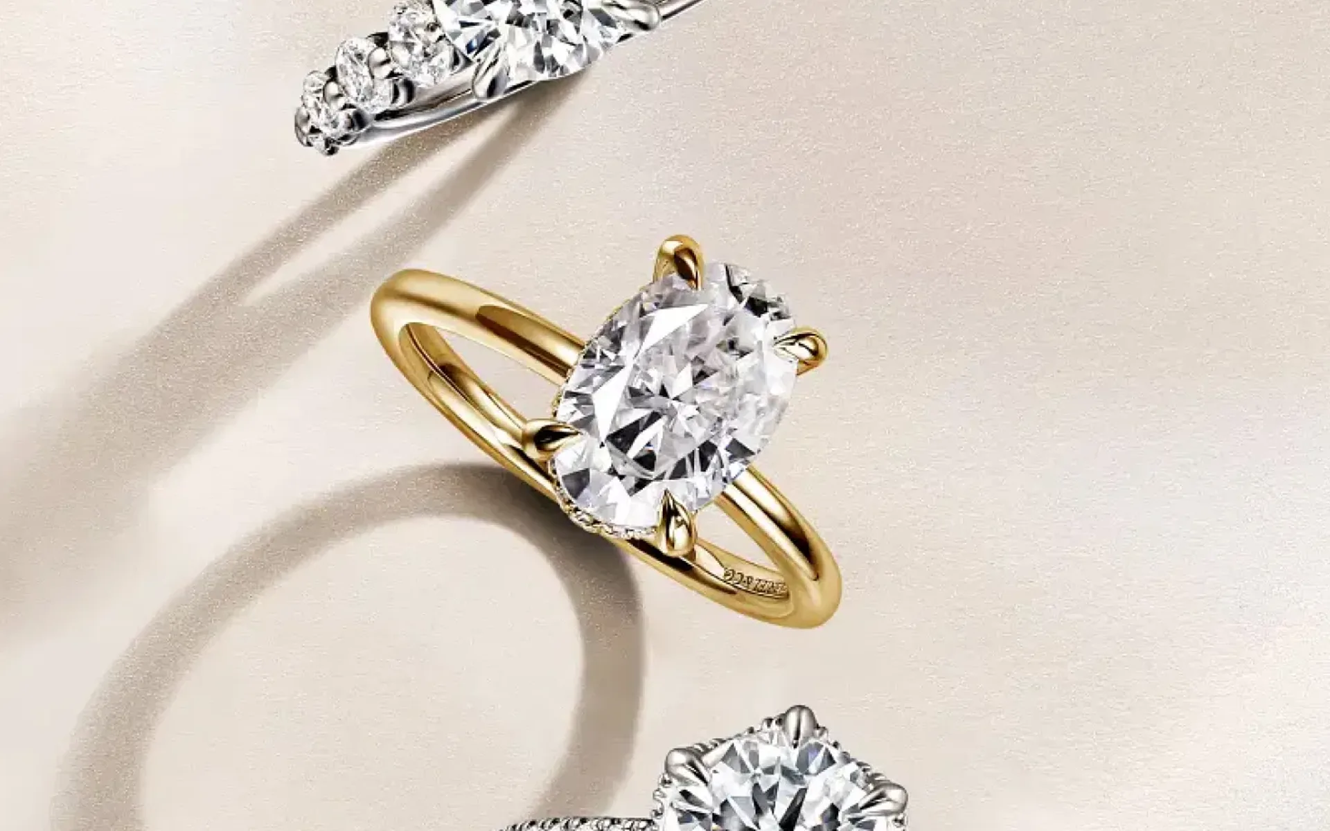 Three diamond engagement rings in different settings on a cream surface