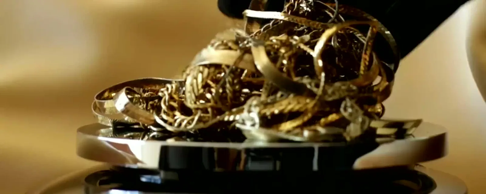 A gloved hand pouring old gold chains onto a jeweler's scale